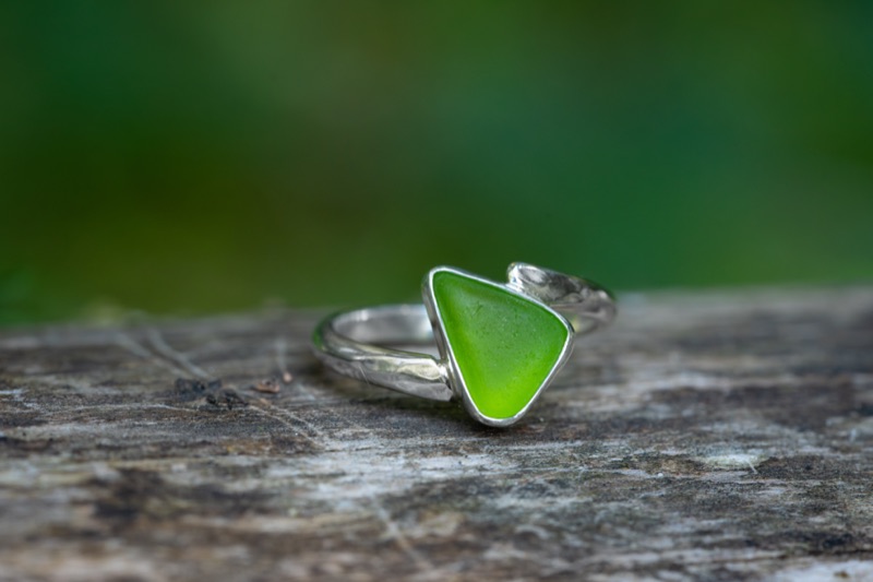 A bright green piece of beach-found sea glass bezel-set on a slim sterling silver bypass band.
